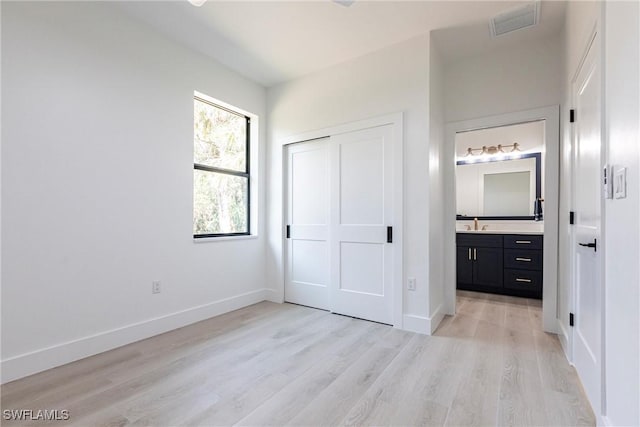 unfurnished bedroom featuring connected bathroom, sink, light hardwood / wood-style flooring, and a closet