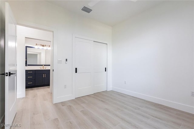 unfurnished bedroom featuring connected bathroom, sink, light hardwood / wood-style floors, and a closet