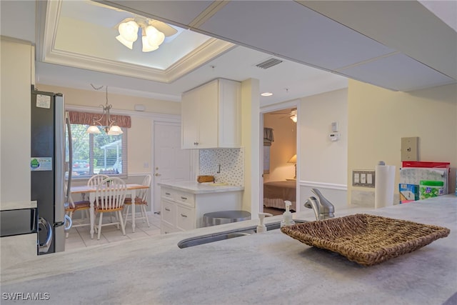 kitchen with light tile patterned flooring, stainless steel refrigerator, tasteful backsplash, a notable chandelier, and a raised ceiling