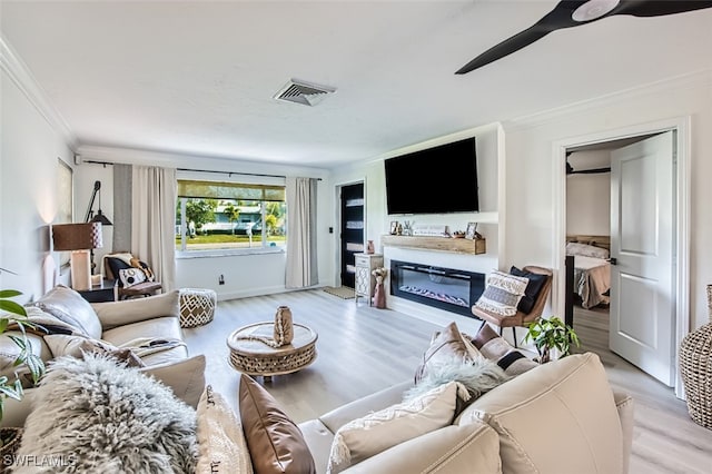 living room with ornamental molding, ceiling fan, and light wood-type flooring