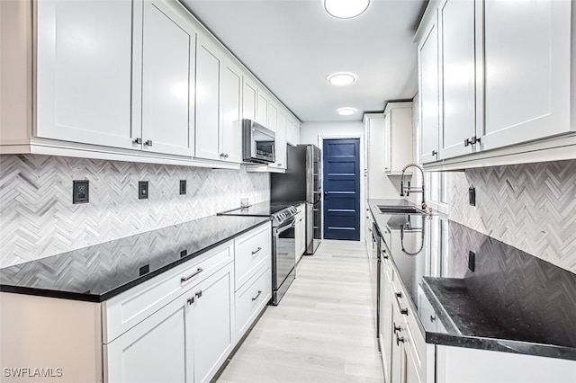 kitchen featuring sink, appliances with stainless steel finishes, white cabinetry, light hardwood / wood-style floors, and decorative backsplash