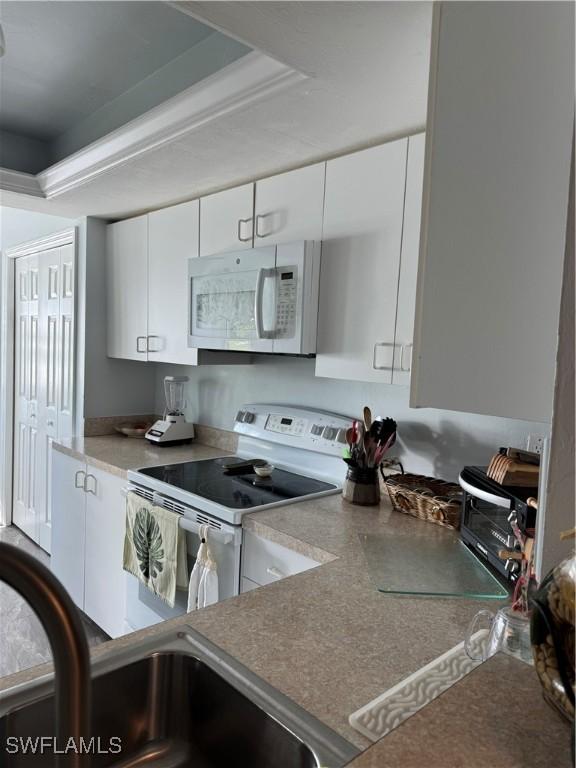 kitchen with white cabinetry, sink, white appliances, and a tray ceiling