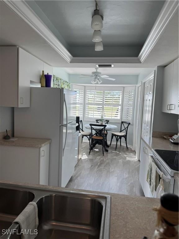 kitchen featuring ceiling fan, white appliances, a raised ceiling, and white cabinets