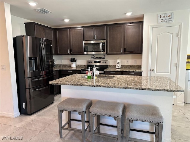 kitchen featuring stainless steel appliances, light stone countertops, sink, and a center island with sink