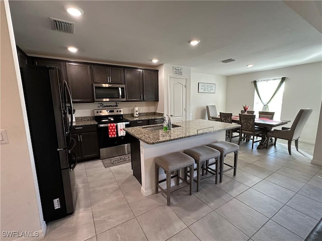 kitchen with appliances with stainless steel finishes, sink, a kitchen breakfast bar, a kitchen island with sink, and light stone countertops