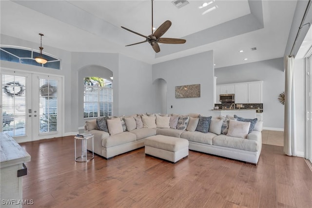 living room with french doors, ceiling fan, a tray ceiling, and light hardwood / wood-style flooring