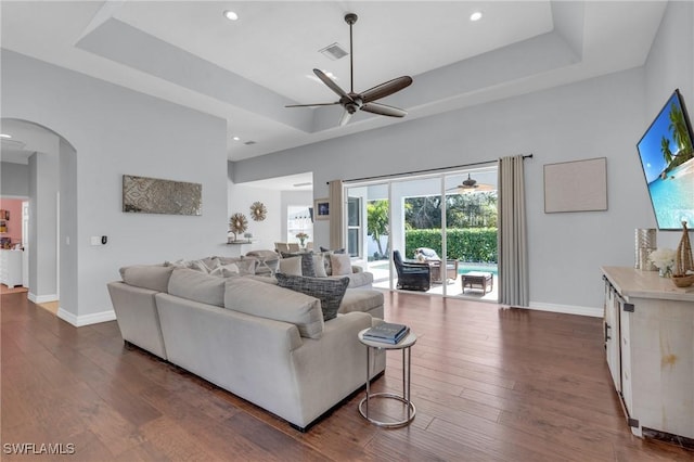 living room featuring ceiling fan, a tray ceiling, and dark hardwood / wood-style flooring