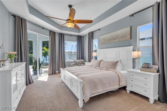 carpeted bedroom with access to outside, ceiling fan, and a tray ceiling