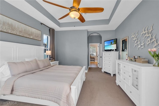 carpeted bedroom featuring ceiling fan and a tray ceiling