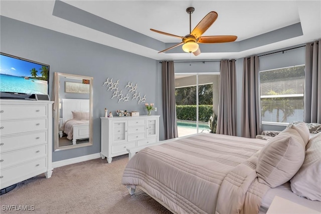 bedroom with a raised ceiling, light colored carpet, access to exterior, and ceiling fan