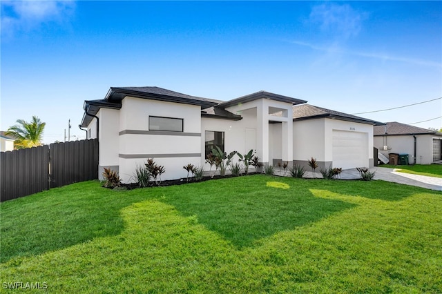 prairie-style house with a front yard, concrete driveway, an attached garage, and fence