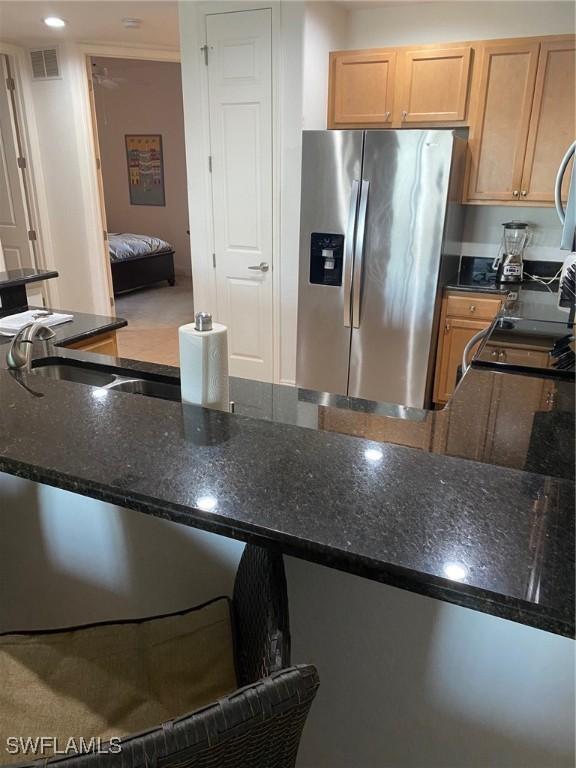 kitchen featuring sink, light brown cabinetry, stainless steel fridge with ice dispenser, and dark stone countertops