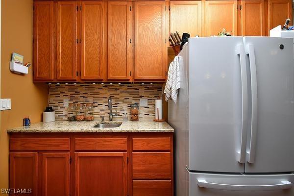 kitchen featuring freestanding refrigerator, brown cabinets, a sink, and decorative backsplash