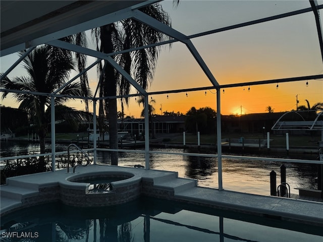 pool at dusk featuring an in ground hot tub and a lanai