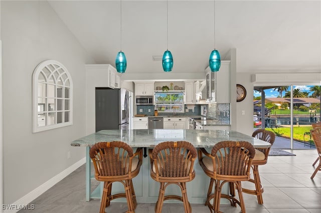 kitchen featuring appliances with stainless steel finishes, dark stone counters, white cabinets, hanging light fixtures, and tasteful backsplash