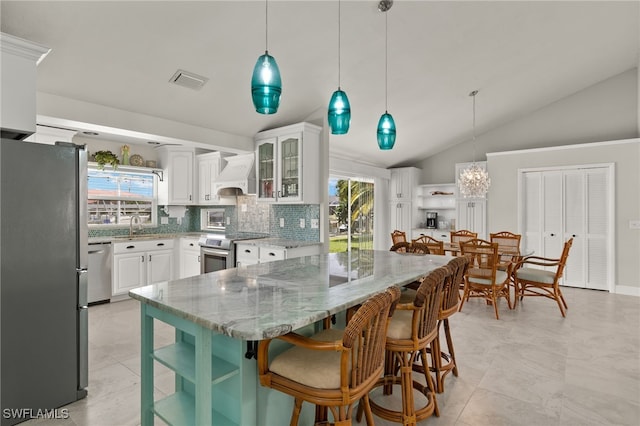 kitchen featuring appliances with stainless steel finishes, hanging light fixtures, premium range hood, light stone counters, and white cabinets