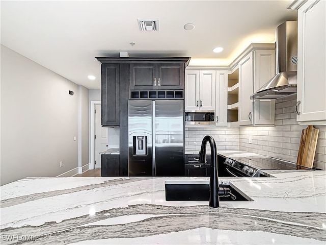 kitchen featuring stainless steel appliances, tasteful backsplash, light stone counters, white cabinets, and wall chimney exhaust hood