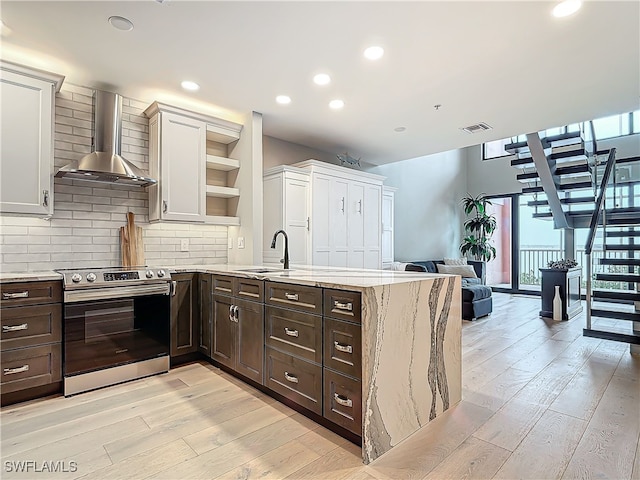 kitchen with wall chimney range hood, electric range, tasteful backsplash, white cabinets, and kitchen peninsula