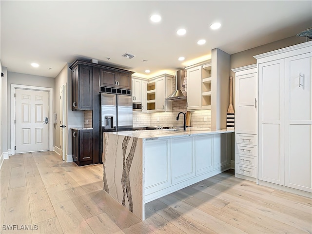 kitchen featuring wall chimney range hood, sink, dark brown cabinets, and kitchen peninsula