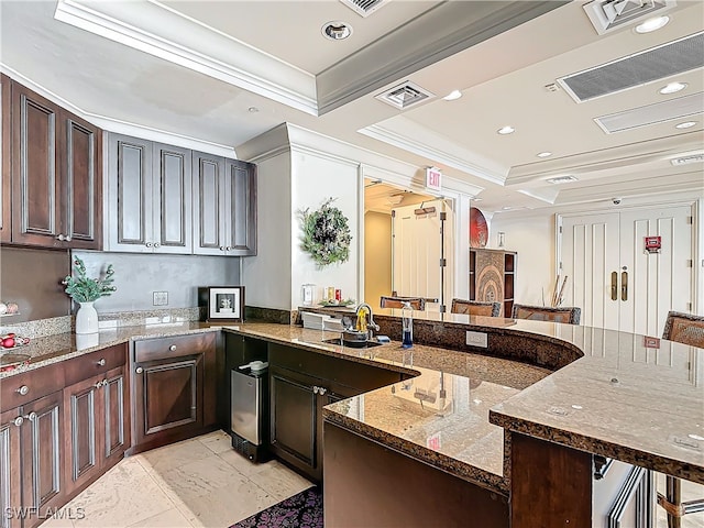 kitchen featuring dark brown cabinetry, a kitchen bar, crown molding, dark stone countertops, and a tray ceiling