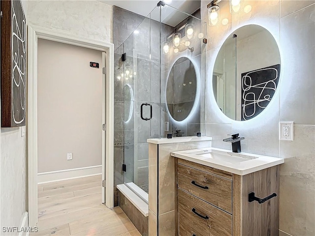 bathroom featuring hardwood / wood-style flooring, vanity, a shower with door, and tile walls