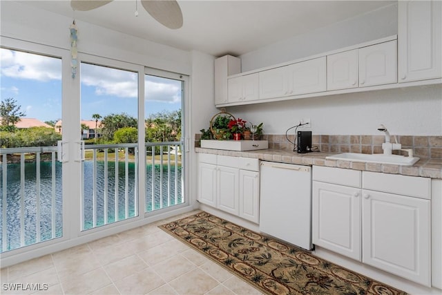 kitchen with white dishwasher, sink, white cabinetry, and a water view