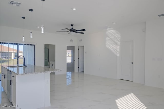 kitchen with sink, a kitchen island with sink, hanging light fixtures, light stone counters, and white cabinets