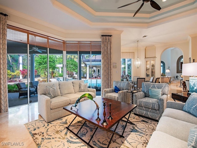 living room featuring arched walkways, a raised ceiling, ceiling fan, and ornamental molding