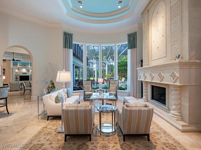 living room with ceiling fan, a high ceiling, a tray ceiling, a fireplace, and ornamental molding