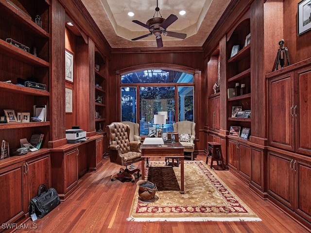 office area with built in shelves, ceiling fan, wooden walls, and light hardwood / wood-style flooring