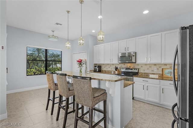 kitchen with white cabinetry, a center island with sink, appliances with stainless steel finishes, pendant lighting, and dark stone counters