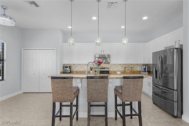 kitchen with pendant lighting, appliances with stainless steel finishes, a kitchen island with sink, and white cabinets