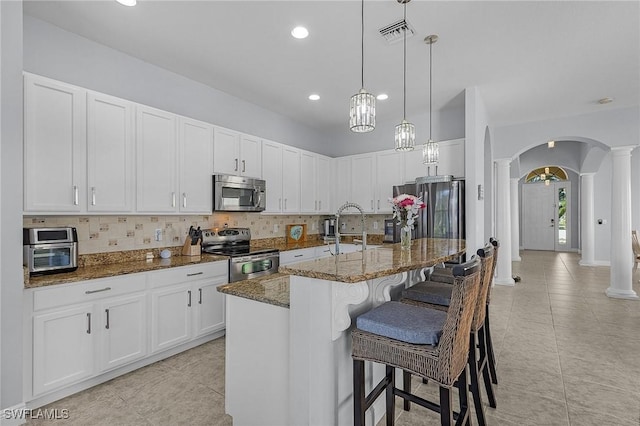 kitchen with an island with sink, appliances with stainless steel finishes, white cabinets, and dark stone counters