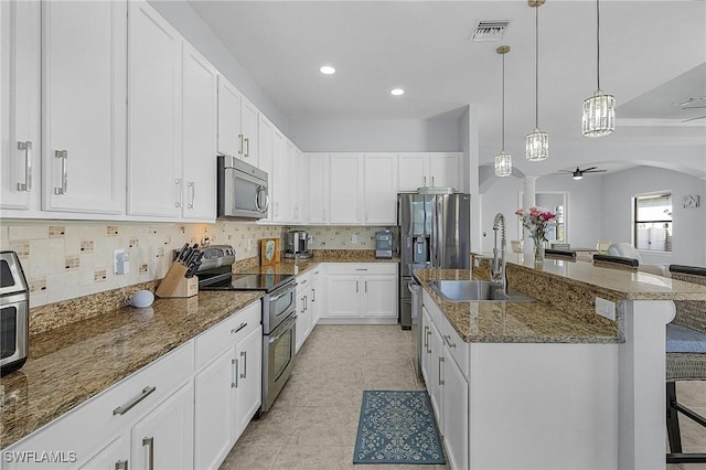 kitchen featuring white cabinetry, dark stone counters, a kitchen breakfast bar, ceiling fan, and stainless steel appliances