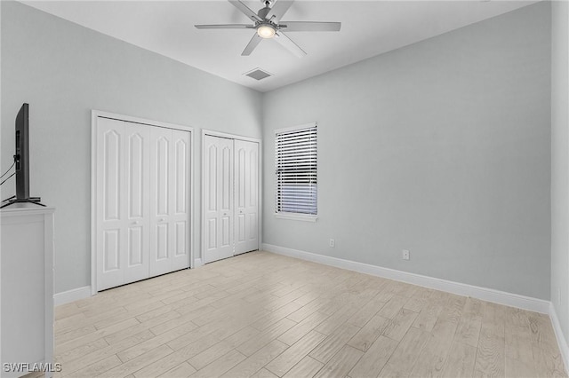 unfurnished bedroom featuring ceiling fan, light wood-type flooring, and two closets