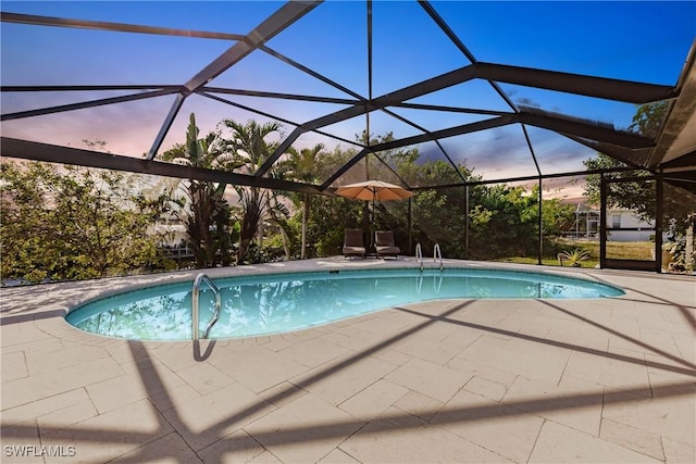 pool at dusk with glass enclosure and a patio