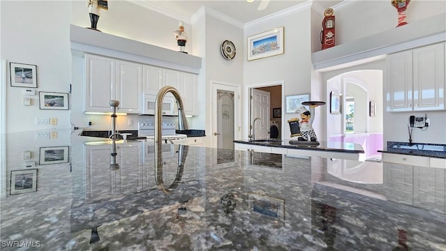 kitchen with sink, white cabinetry, ornamental molding, dark stone counters, and stove