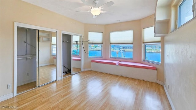 unfurnished bedroom featuring multiple windows, two closets, ceiling fan, and light hardwood / wood-style flooring