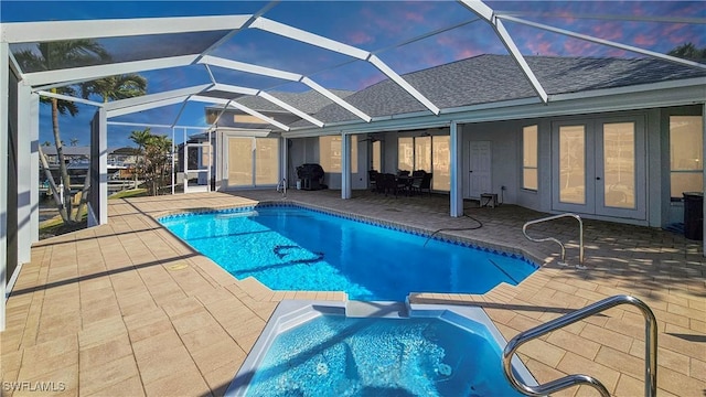 pool at dusk with glass enclosure and a patio area