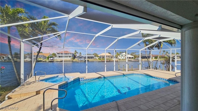 pool at dusk with a water view, an in ground hot tub, a lanai, and a patio