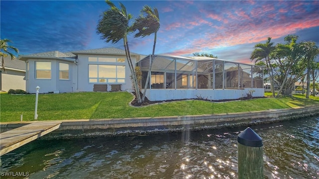 back house at dusk featuring a water view, a lanai, and a yard