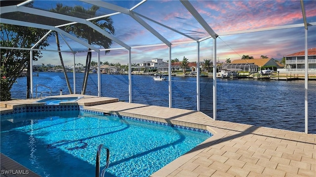 pool at dusk with a lanai, a water view, and an in ground hot tub