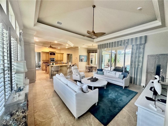 living area with visible vents, a tray ceiling, a ceiling fan, and crown molding