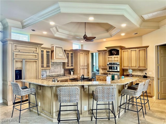 kitchen featuring a spacious island, glass insert cabinets, light stone countertops, premium range hood, and a kitchen bar