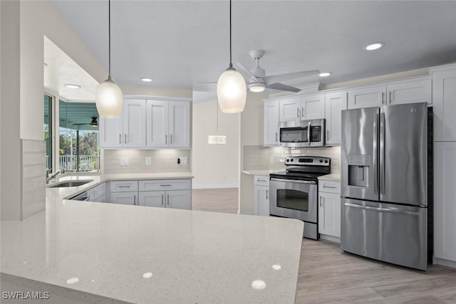 kitchen featuring sink, light wood-type flooring, appliances with stainless steel finishes, pendant lighting, and white cabinets