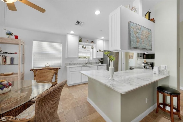 kitchen featuring sink, stainless steel appliances, white cabinets, a kitchen bar, and kitchen peninsula