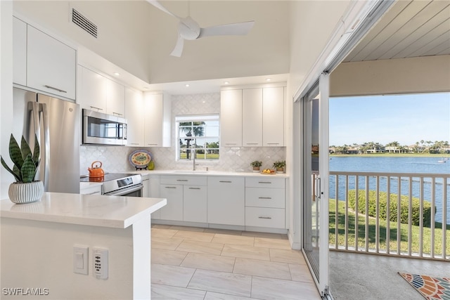 kitchen with sink, white cabinetry, stainless steel appliances, a water view, and kitchen peninsula