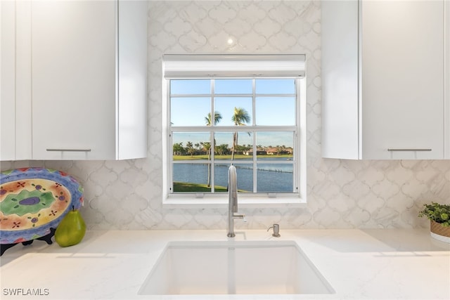 room details featuring a water view, white cabinetry, sink, and tasteful backsplash