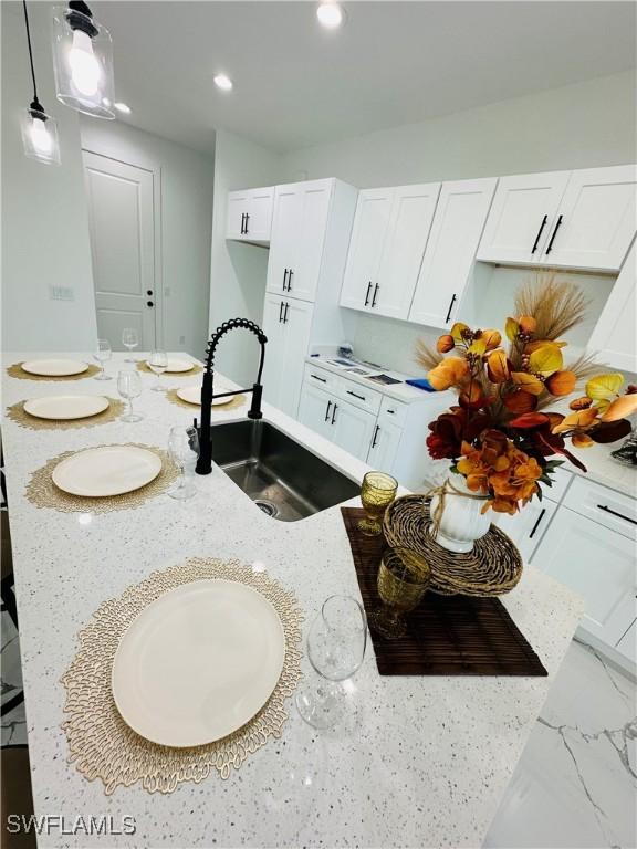 kitchen featuring light stone counters, decorative light fixtures, sink, and white cabinets