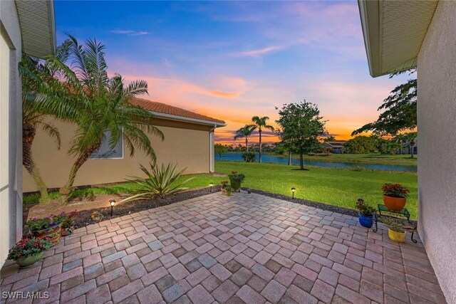 patio terrace at dusk featuring a water view and a yard